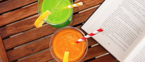 Dos bebidas con pajitas y rodajas de limón sobre una mesa de madera junto a un libro abierto.