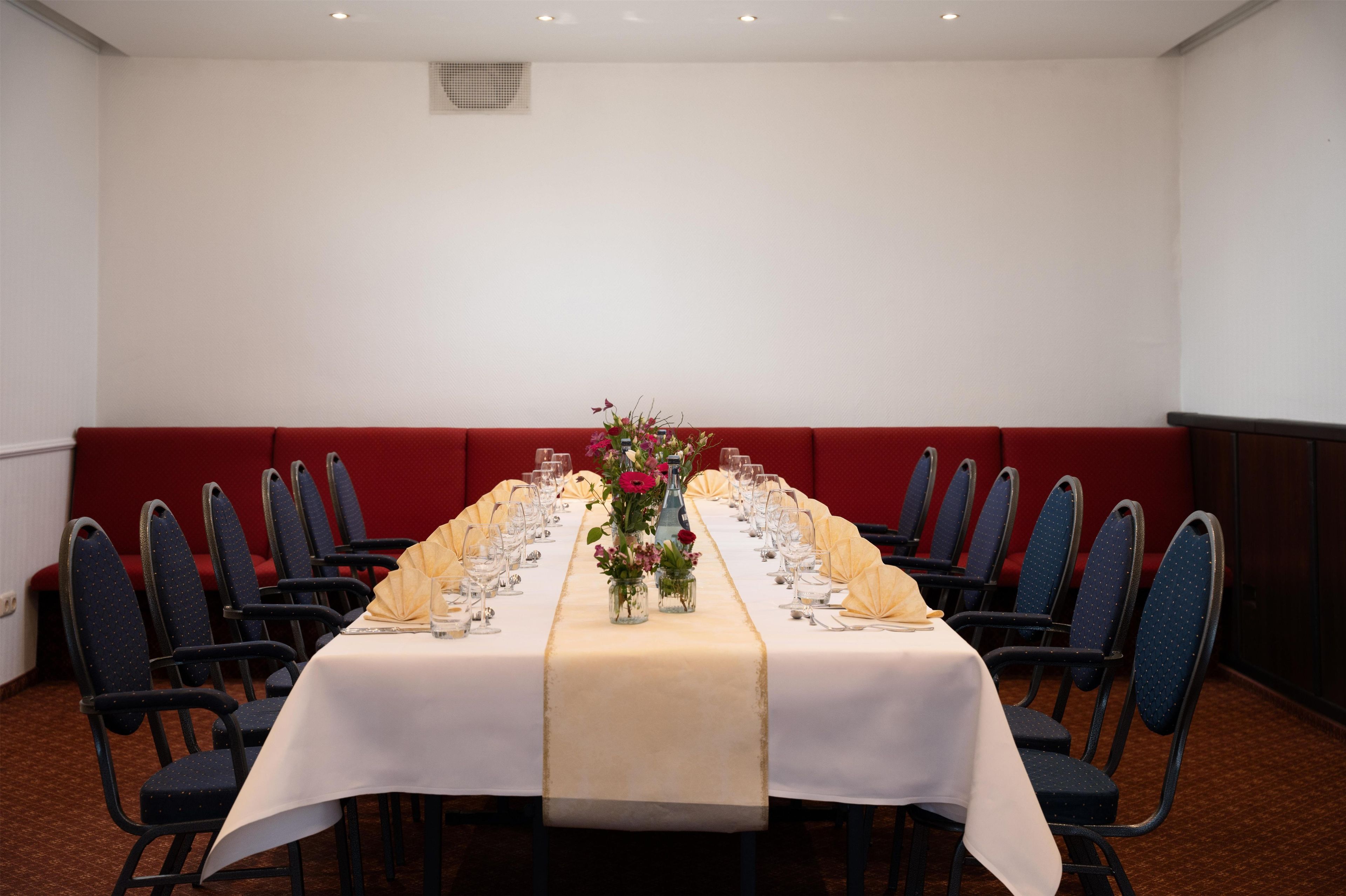 Un salón de conferencias con una larga mesa dispuesta para una reunión, rodeado de sillas.