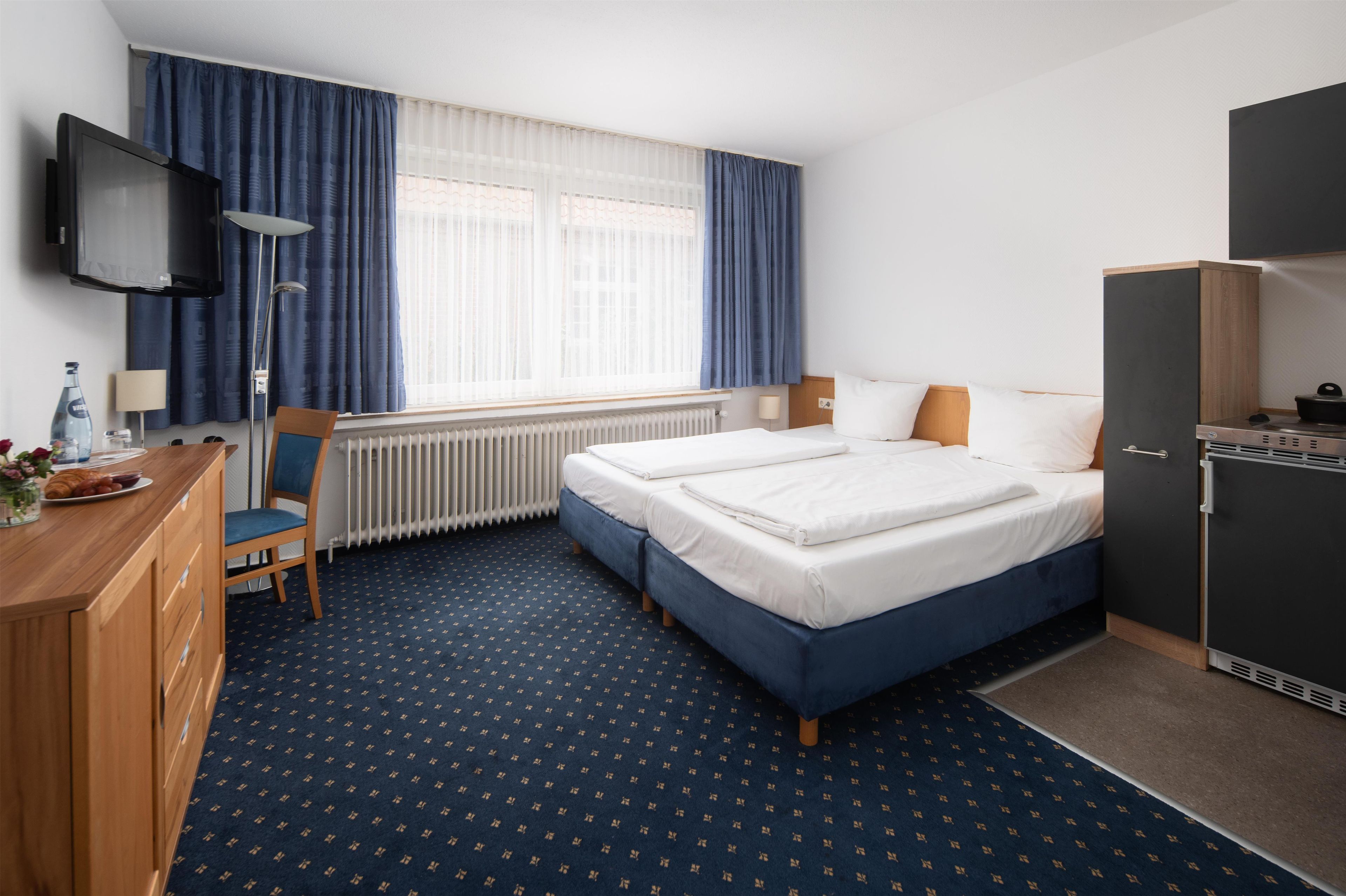 A hotel room with a bed, a desk with a chair, a television, and a kitchenette.