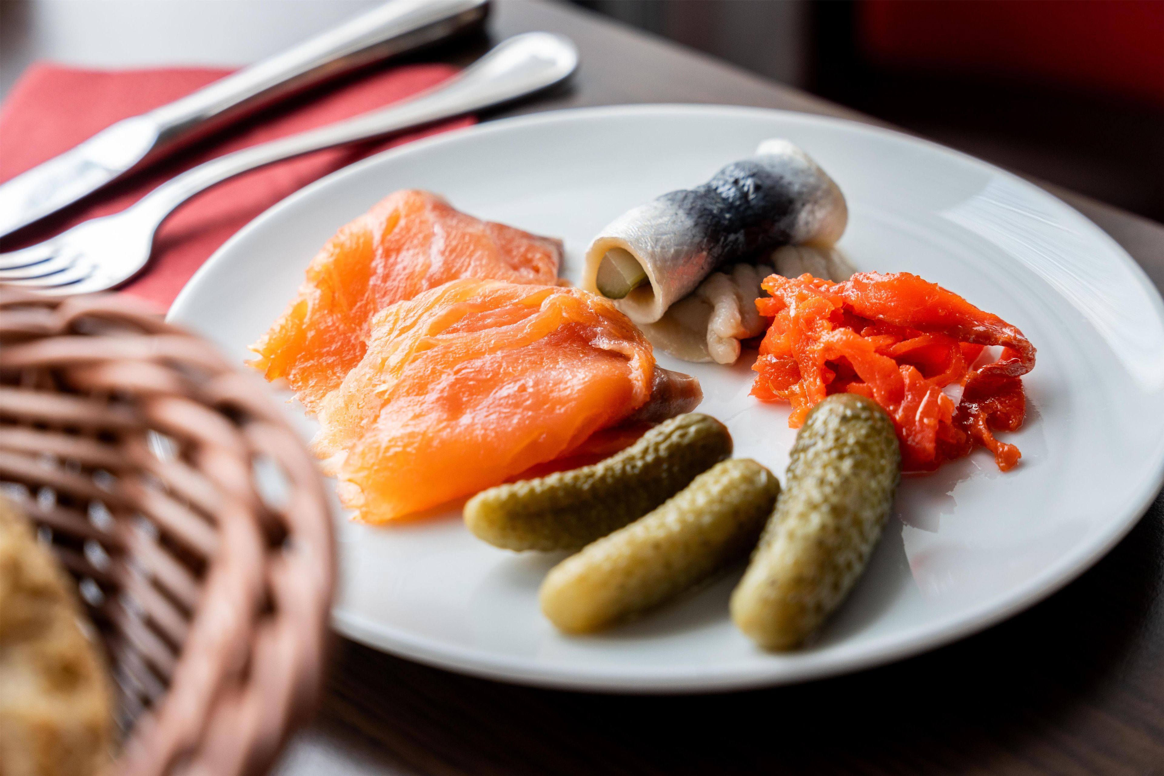 A plate with smoked salmon, pickles, and a small fish.