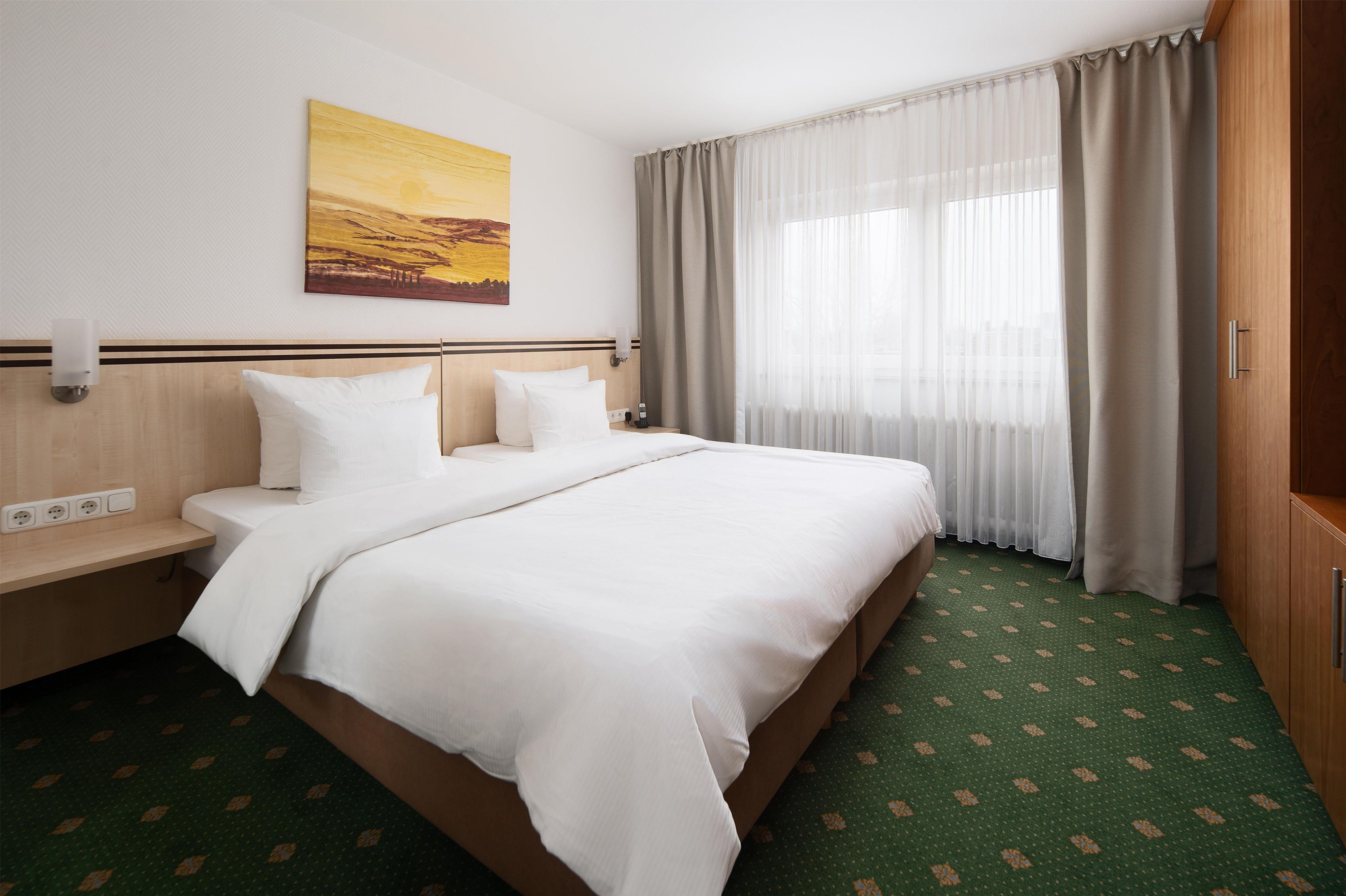 Een hotelkamer met een groot bed, een nachtkastje, een schilderij aan de muur en een raam met gordijnen.
