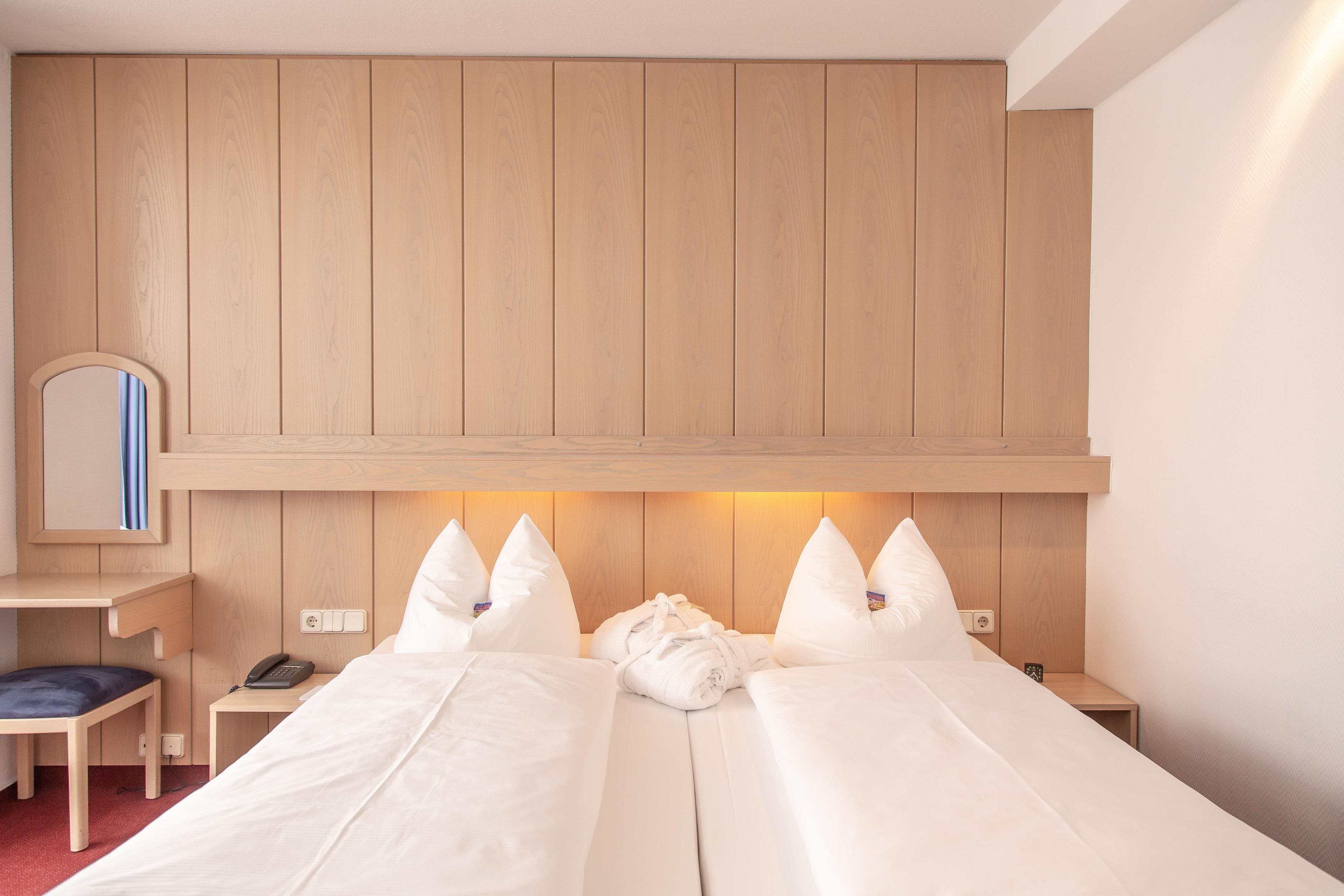 A hotel room with two beds, a desk, a chair, a mirror, and a bedside table with a phone.