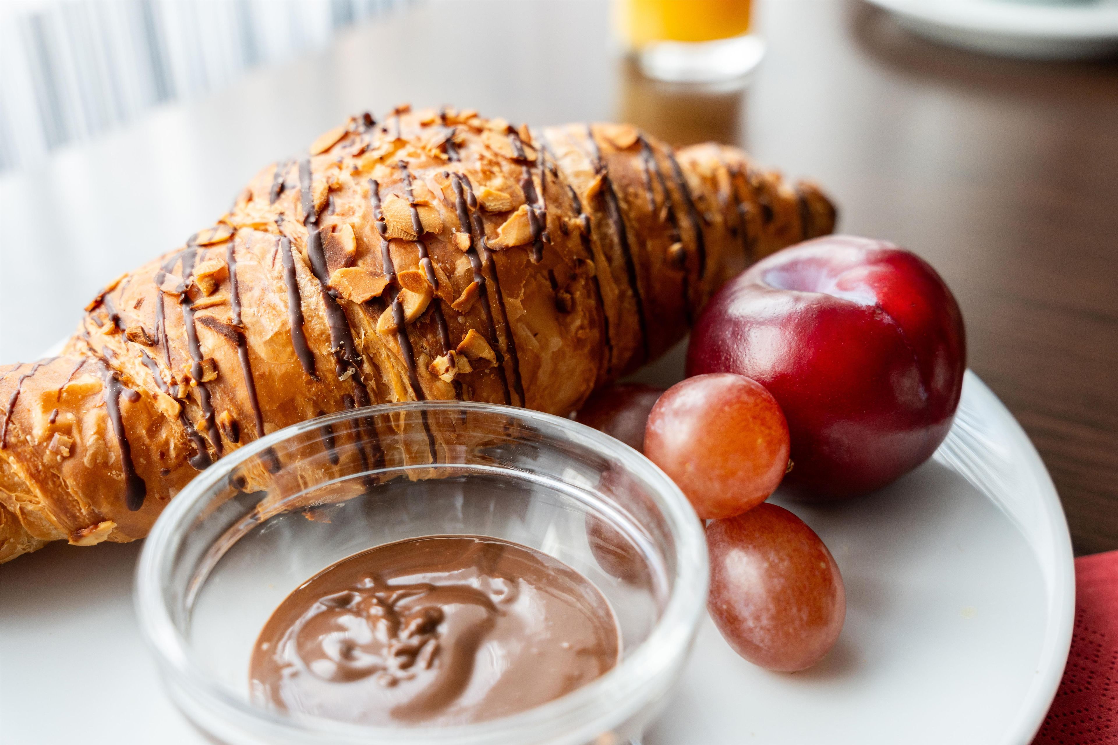 Een croissant, een rode appel en een klein schaaltje chocoladesaus op een bord.