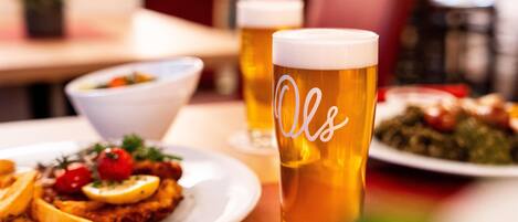Una mesa de comedor con platos de comida y dos vasos de cerveza.