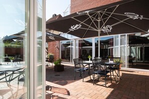 An outdoor patio area with tables and chairs, umbrellas, and potted plants. - Best Western Hotel Heide (Oldenburg)