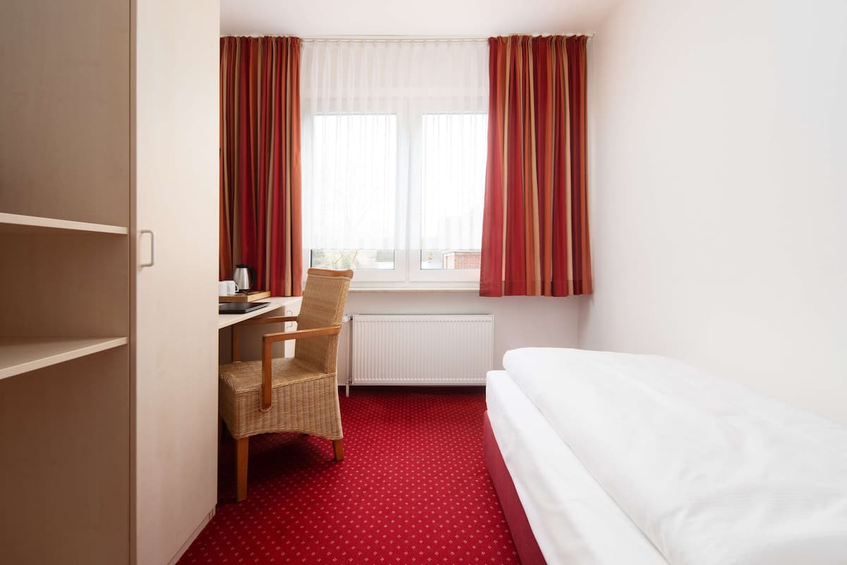 Una habitación de hotel con cama, escritorio y silla, y ventana con cortinas.