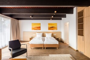 A modern bedroom with a wooden headboard, two beds, a black chair, and artwork on the wall. - Best Western Hotel Heide (Oldenburg)