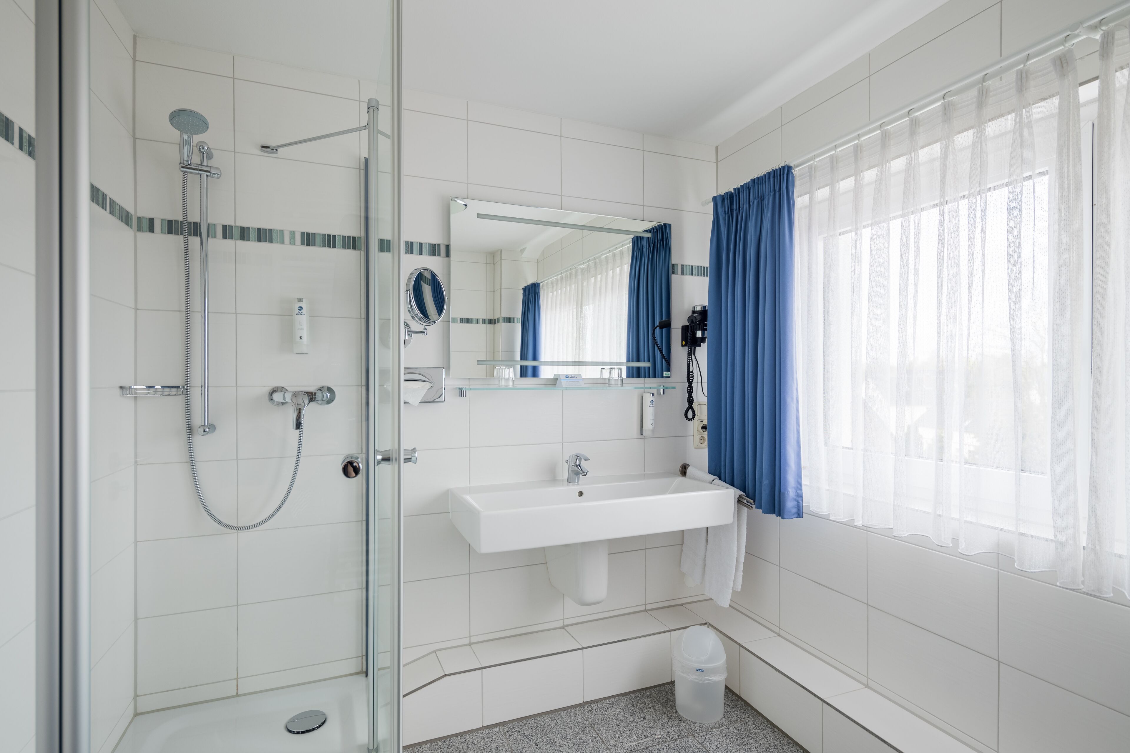A modern bathroom with a glass-enclosed shower, a white sink, and a large mirror.