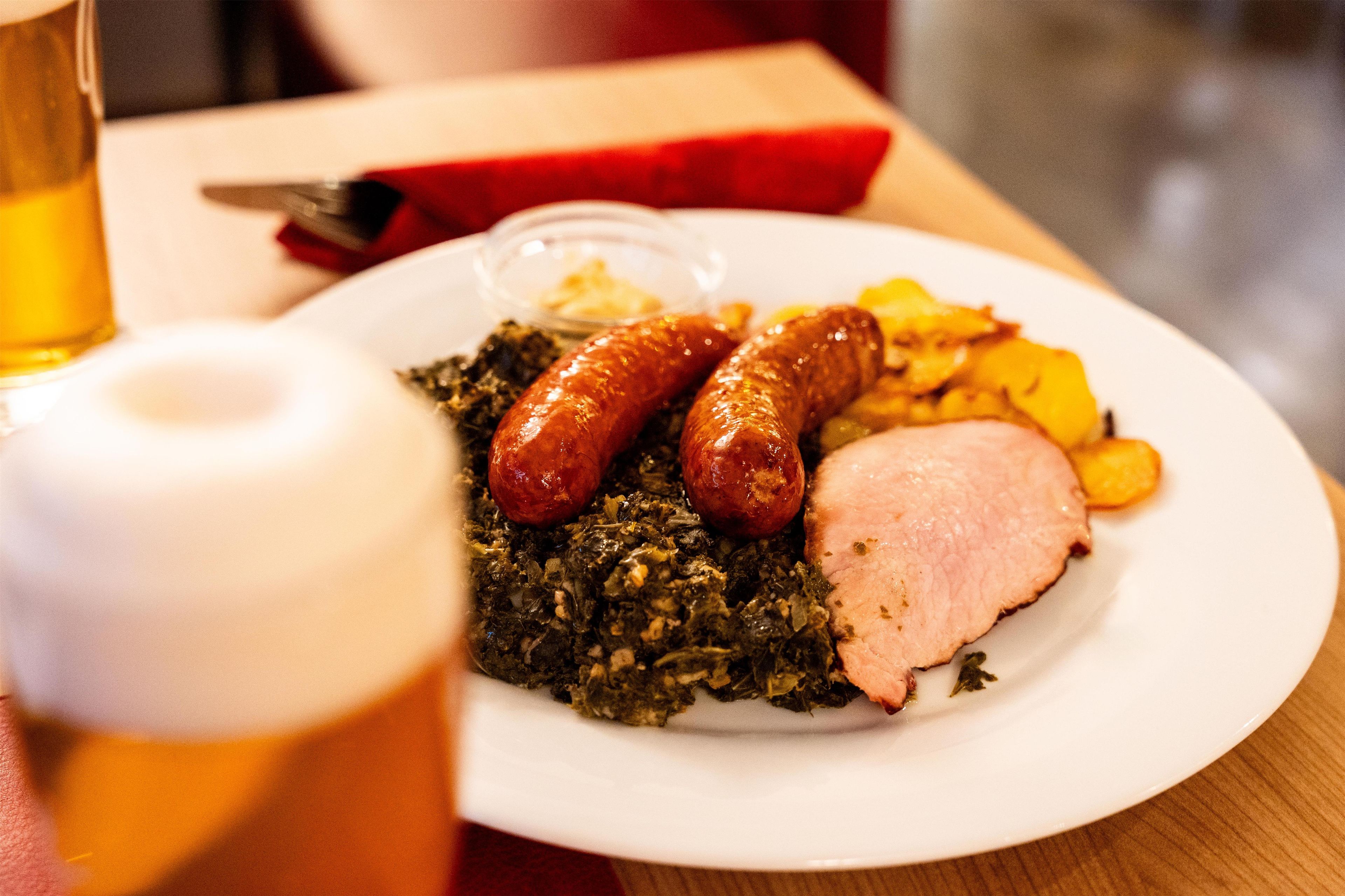 A plate with sausages, greens, and ham.