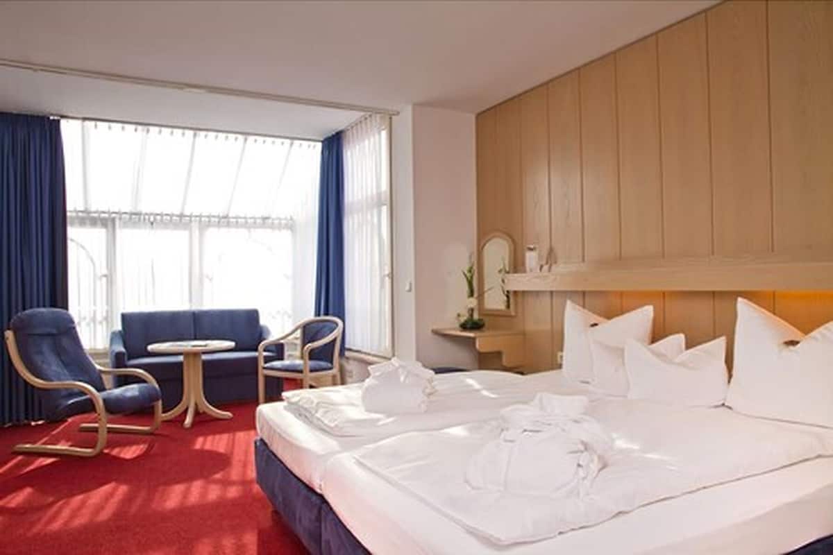 Habitación de hotel con una cama grande, dos sillones, una mesita redonda y un cabecero de madera.