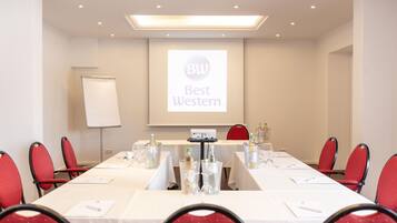 A conference room with a long table, red chairs, and a projector screen displaying 'Best Western' branding.