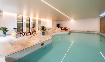 Una piscina interior con borde de azulejos, sillones de descanso y plantas en macetas.