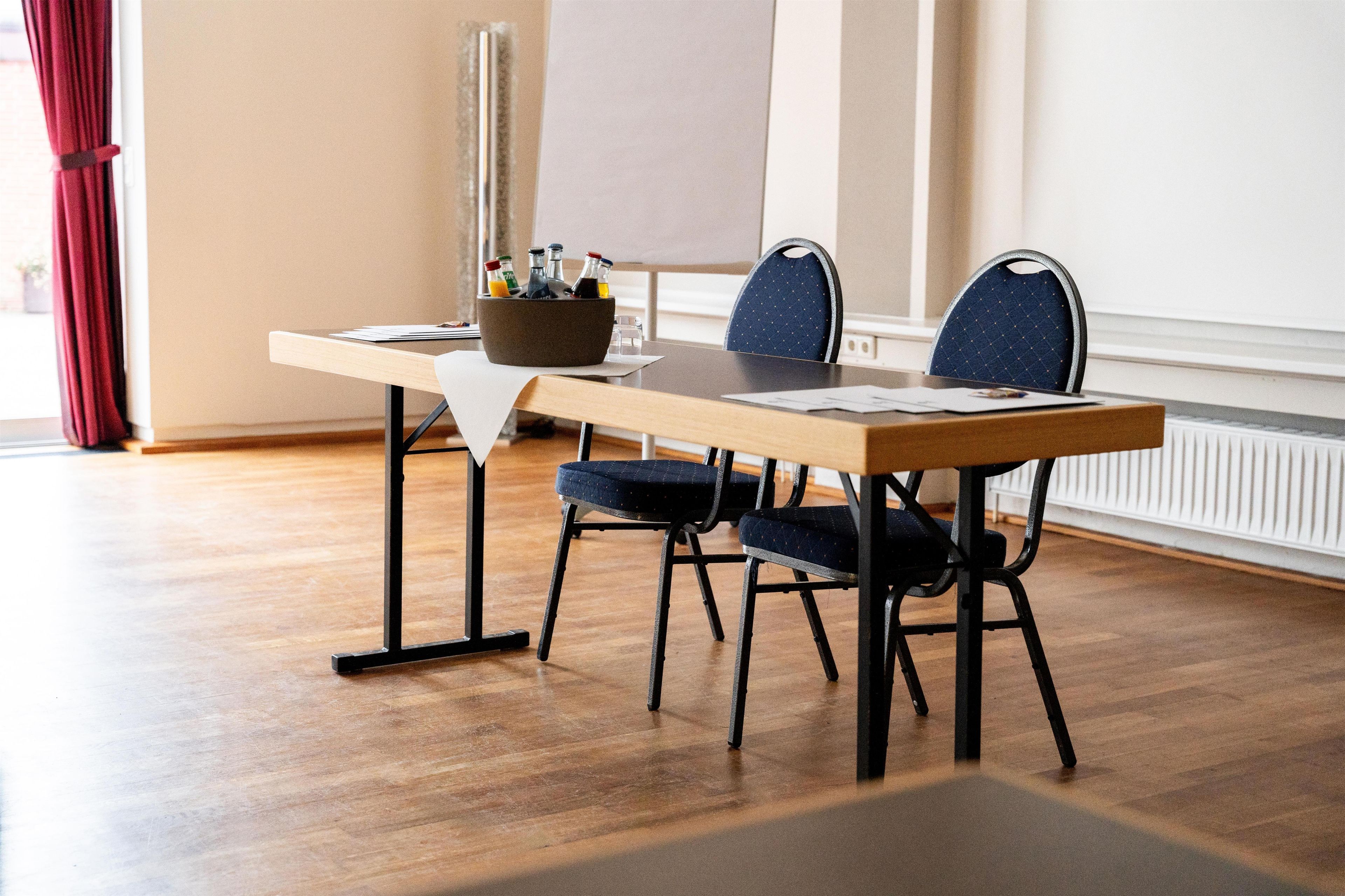 A conference room with a wooden table, two chairs, a whiteboard, and a bottle holder with drinks.