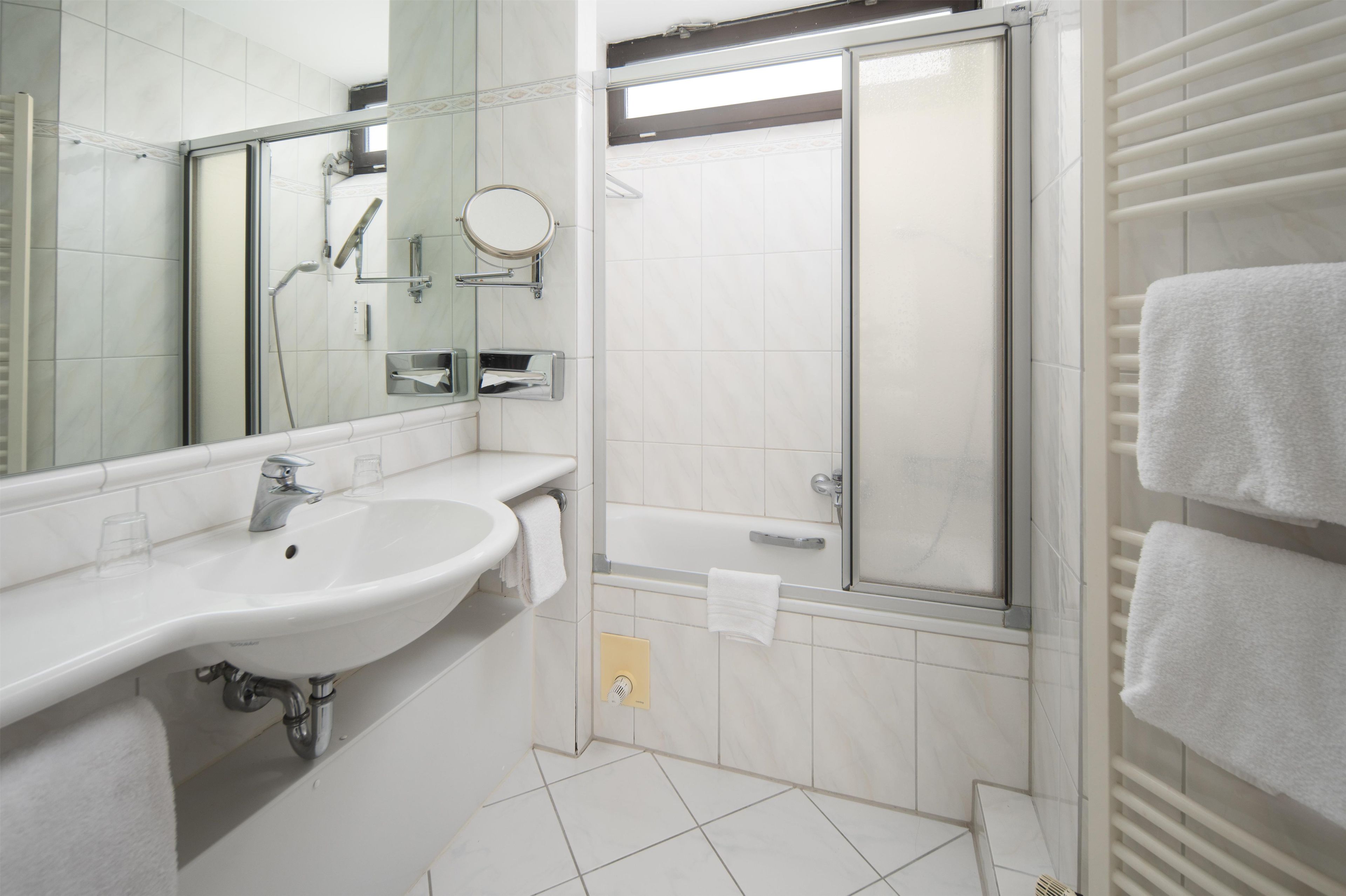 Un baño con lavamanos, espejo, ducha y toallero.