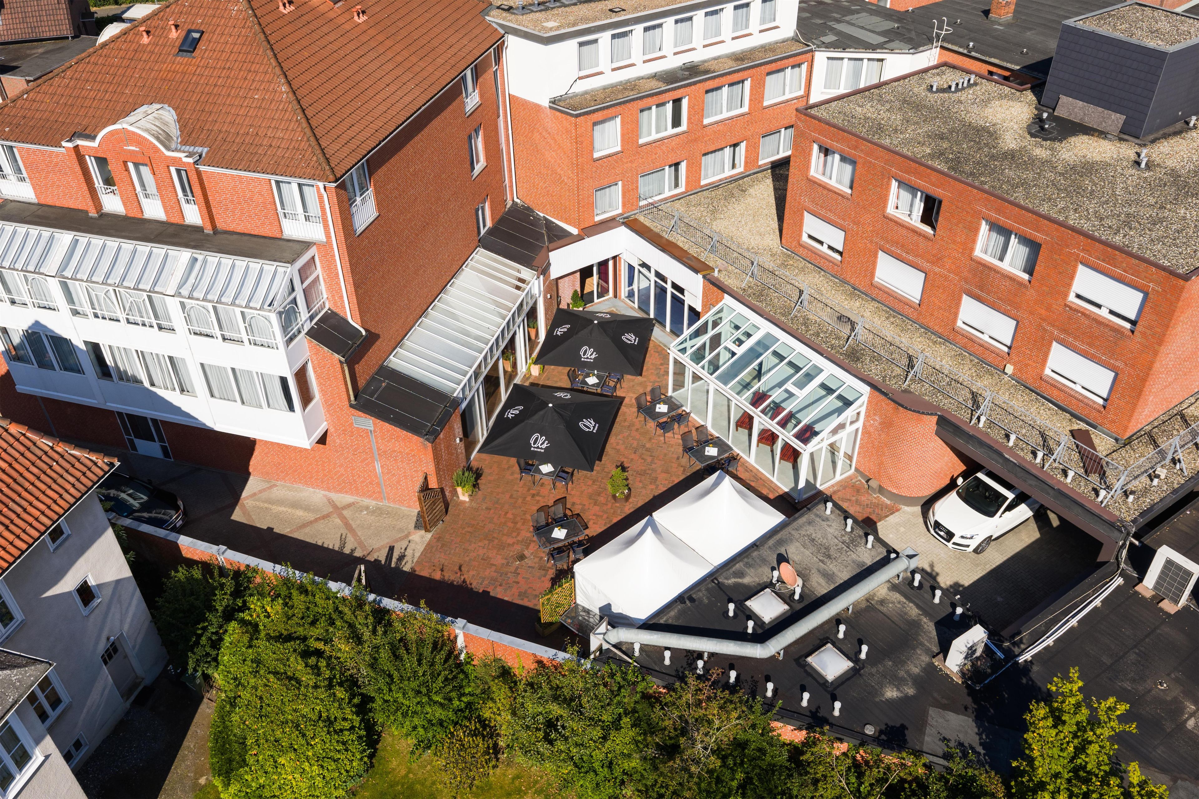 A multi-story building with a courtyard, featuring a covered outdoor seating area with tables and umbrellas, and a rooftop terrace.