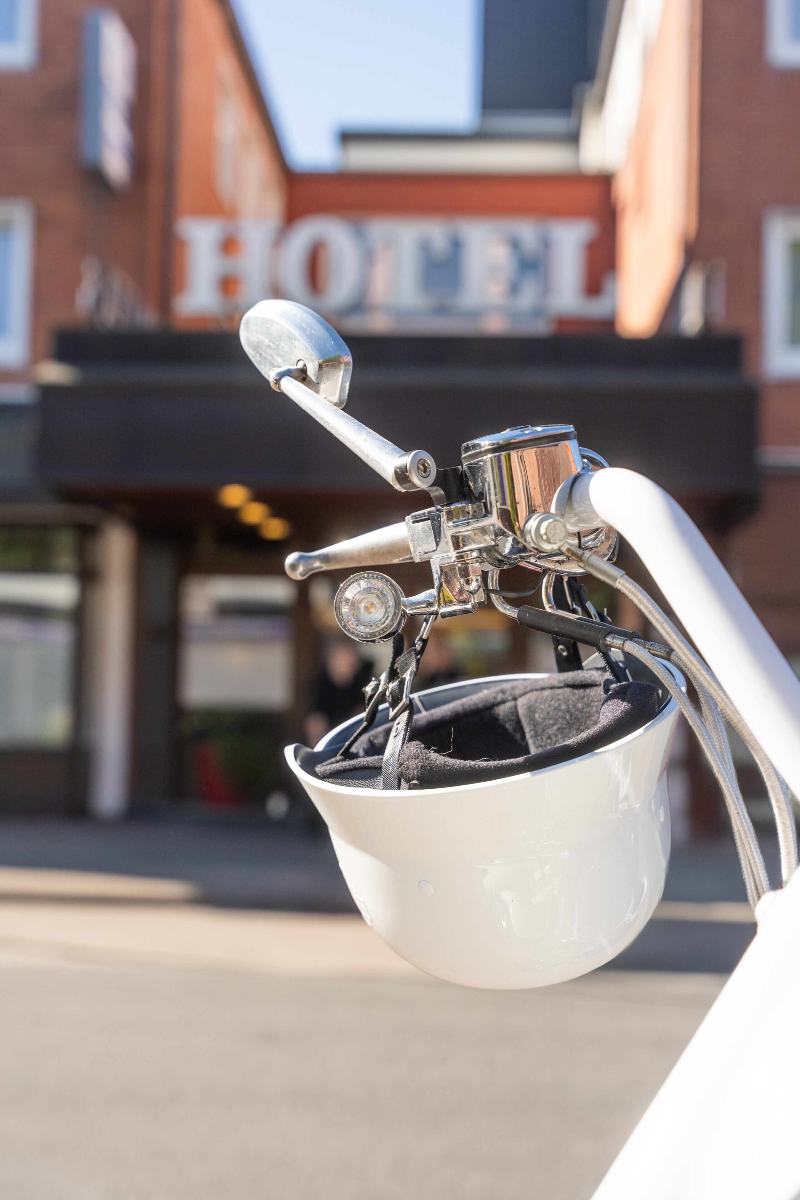 A motorcycle helmet with a handlebar and a mirror, in front of a building with a sign that reads 'HOTEL'.