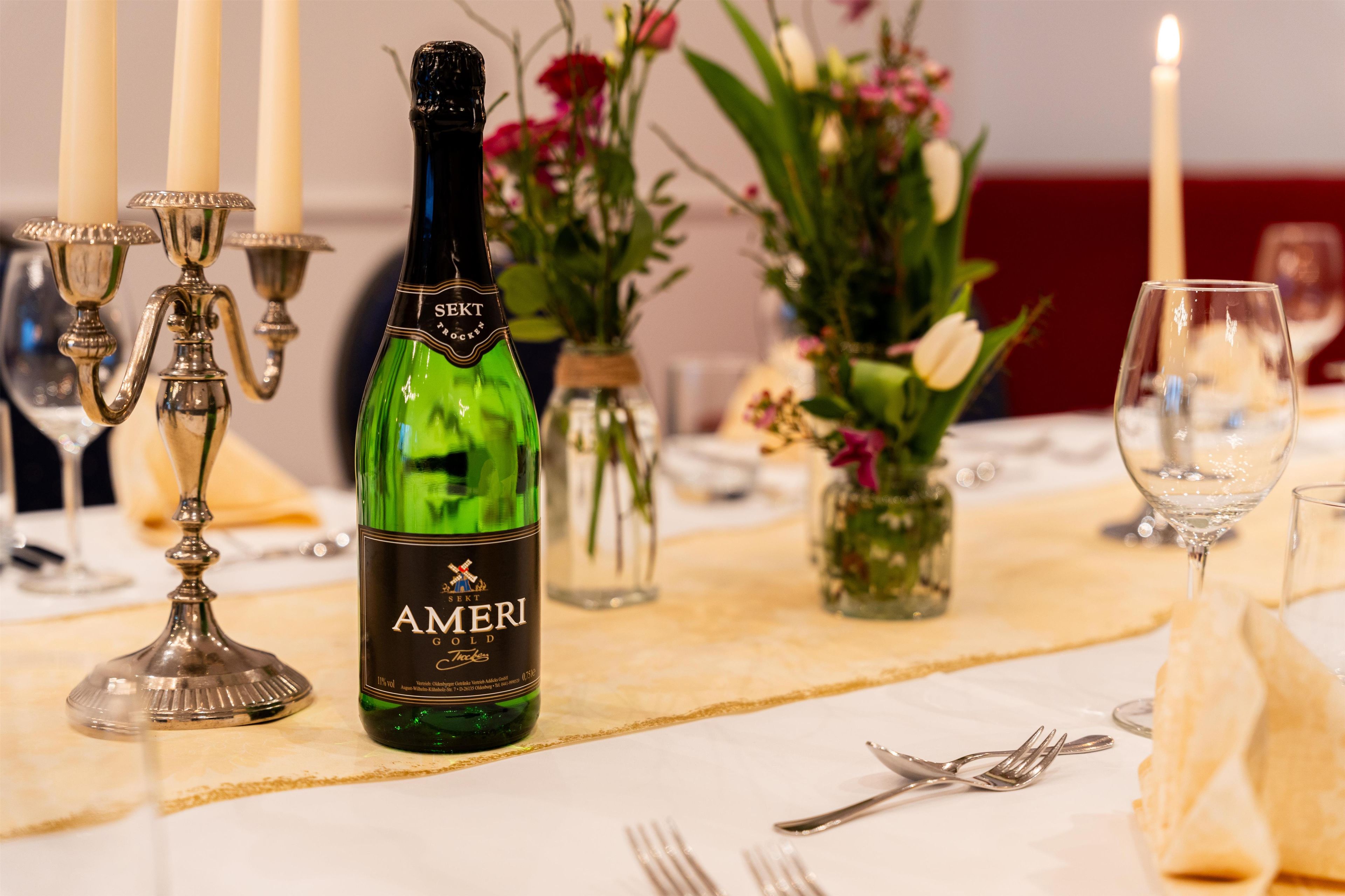 Mesa preparada para cenar con una botella de Amari Golder, velas y arreglos florales.