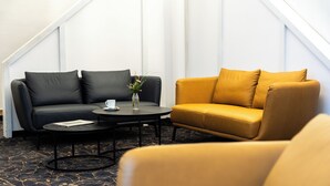 A room with a black sofa, a yellow sofa, a round coffee table, and a vase with flowers. - Best Western Hotel Heide (Oldenburg)