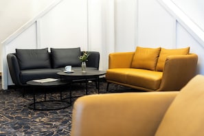 A room with a black sofa, a yellow sofa, a round coffee table, and a vase with flowers. - Best Western Hotel Heide (Oldenburg)