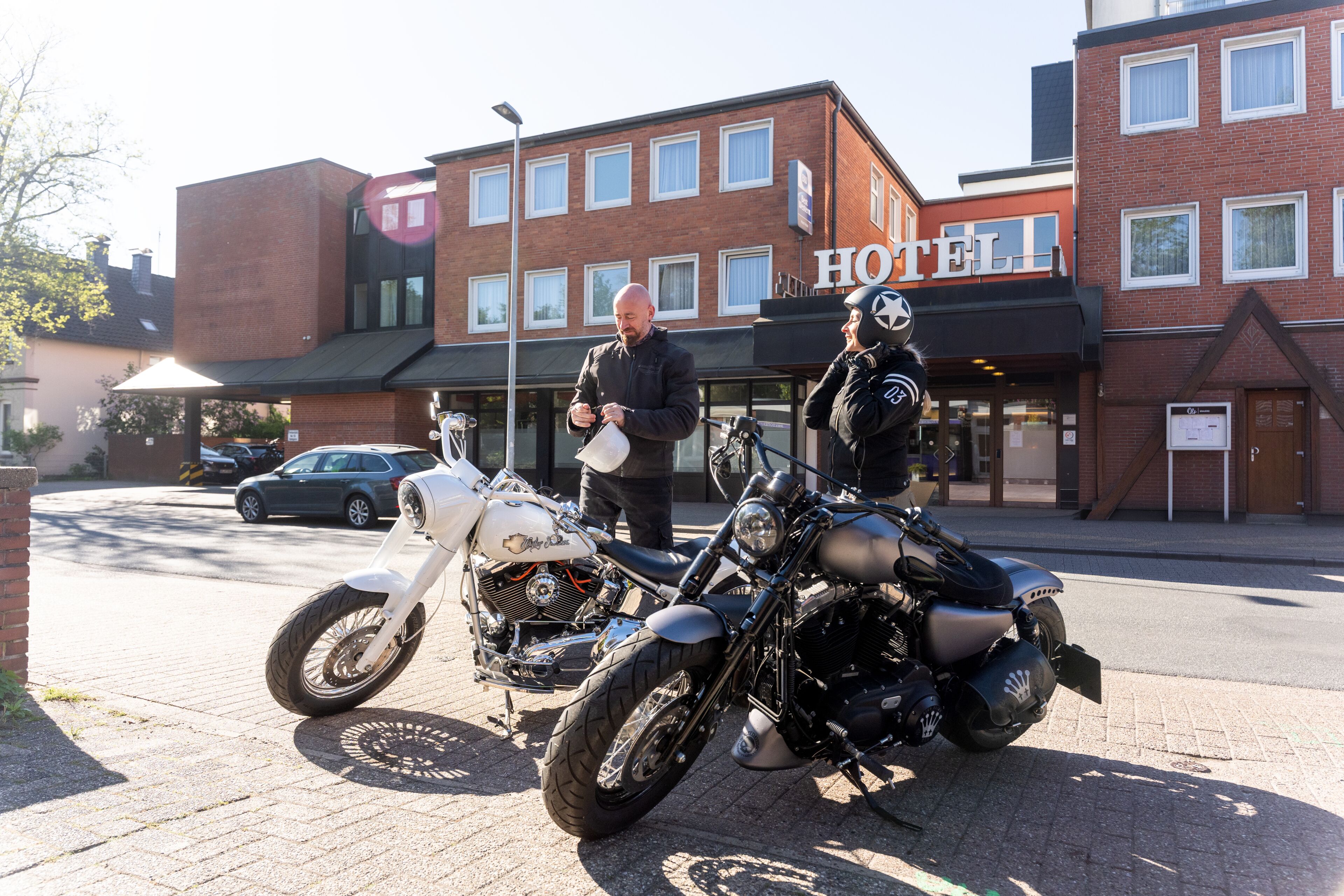 A hotel with a brick facade, a signboard with 'HOTEL' visible, and two motorcycles parked in front.