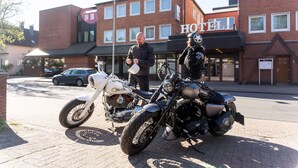A hotel with a brick facade, a signboard with 'HOTEL' visible, and two motorcycles parked in front. - Best Western Hotel Heide (Oldenburg)