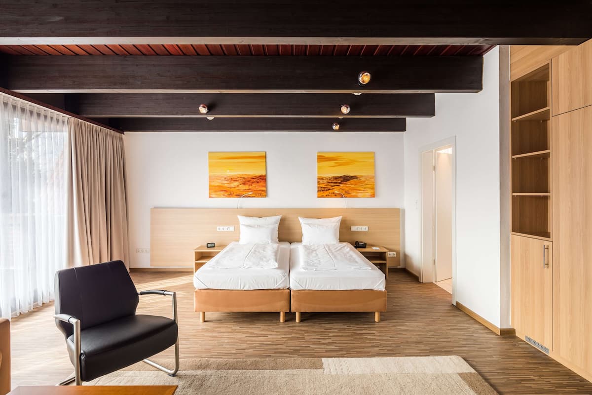 Un dormitorio moderno con suelo de madera, dos camas, una silla negra y armarios de madera.