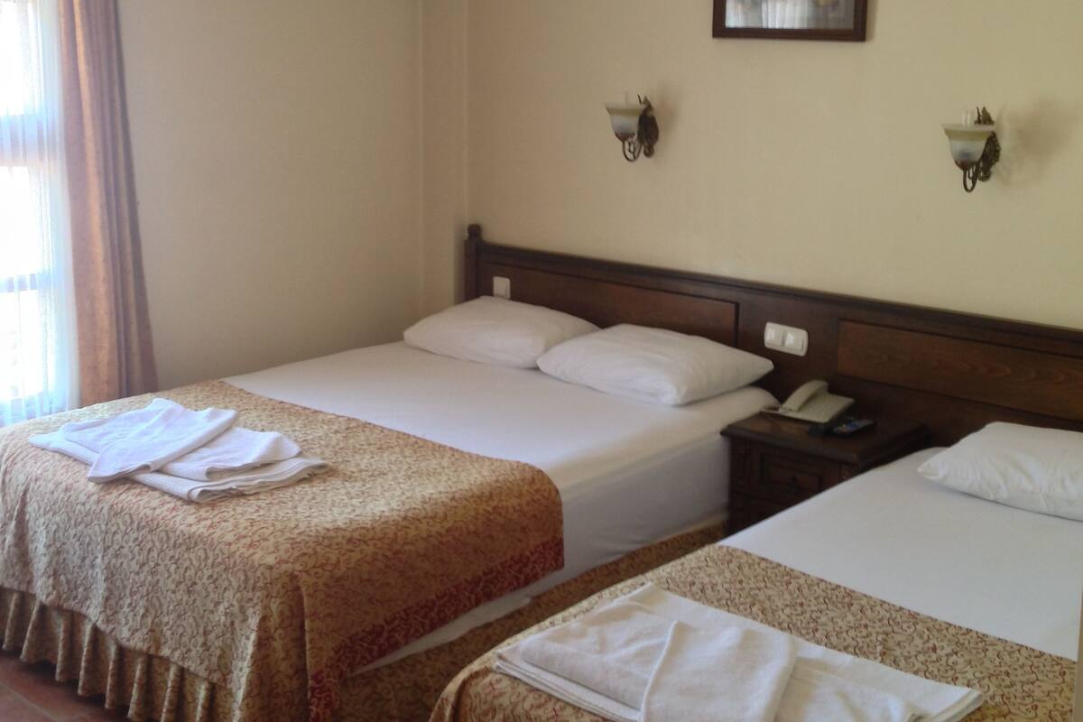 A hotel room with two beds, a nightstand, a telephone, and a wall-mounted light fixture.