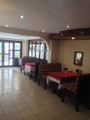 Un restaurant avec des banquettes et des tables, un sol carrelé et une vue sur l’extérieur grâce à de grandes fenêtres.