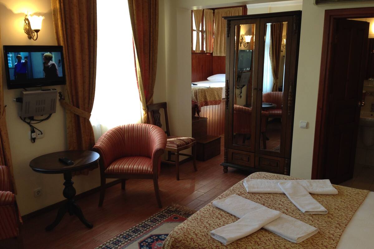 A hotel room with a bed, a chair, a small table, a television, and a wardrobe.