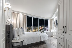Habitación de hotel moderna con una cama grande, un tocador, una bañera y vistas a la ciudad a través de ventanas de gran altura.