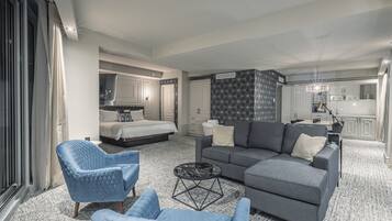 Una habitación de hotel moderna con una cama grande, un sofá gris, un sillón azul y un comedor.