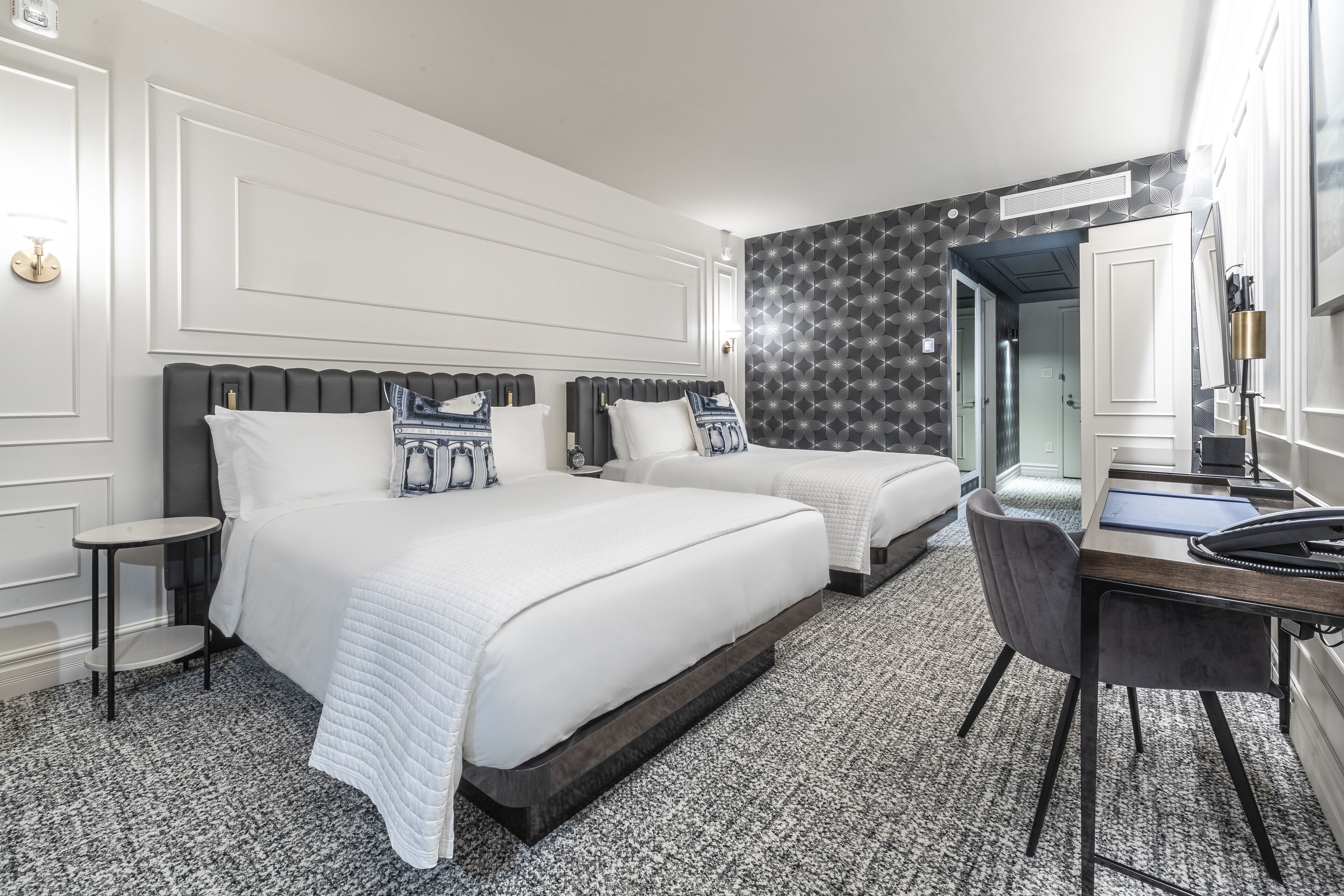 A hotel room with two beds, a desk, and a chair.