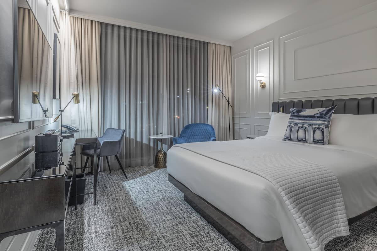 Hotellihuone, jossa on suuri sänky, työpöytä tuolilla, pieni pöytä ja lamppu.