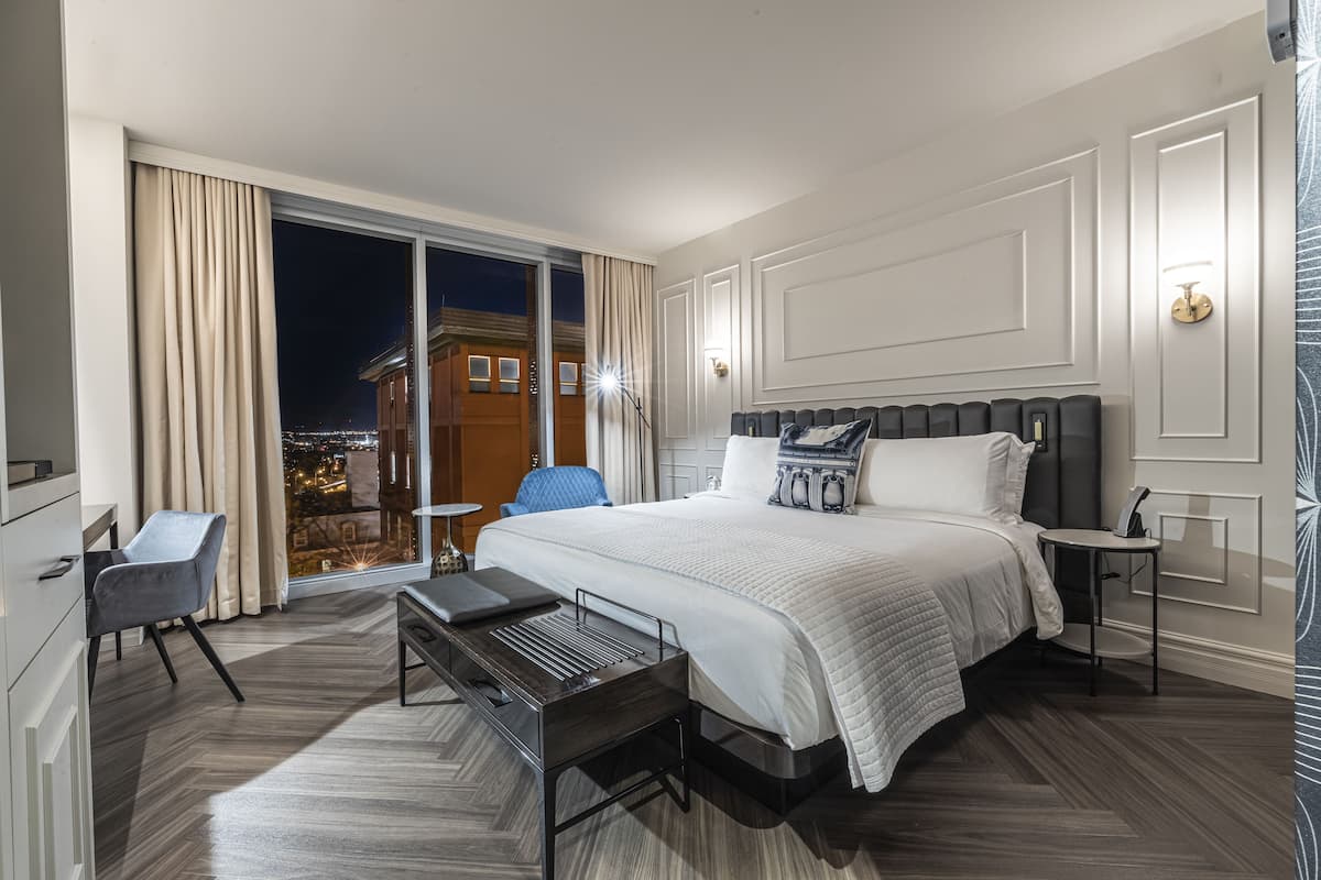 Hotellihuone, jossa on suuri sänky, työpöytä, tuoli ja näkymä kaupunkiin yöllä.