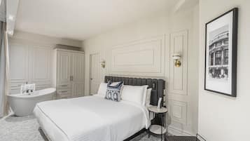 Une chambre à coucher avec un grand lit, une table de chevet, une commode, une lampe fixée au mur, un tableau encadré, une baignoire et une armoire.