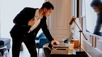 A person working on a laptop in a room with a large window, a desk, and a chair.