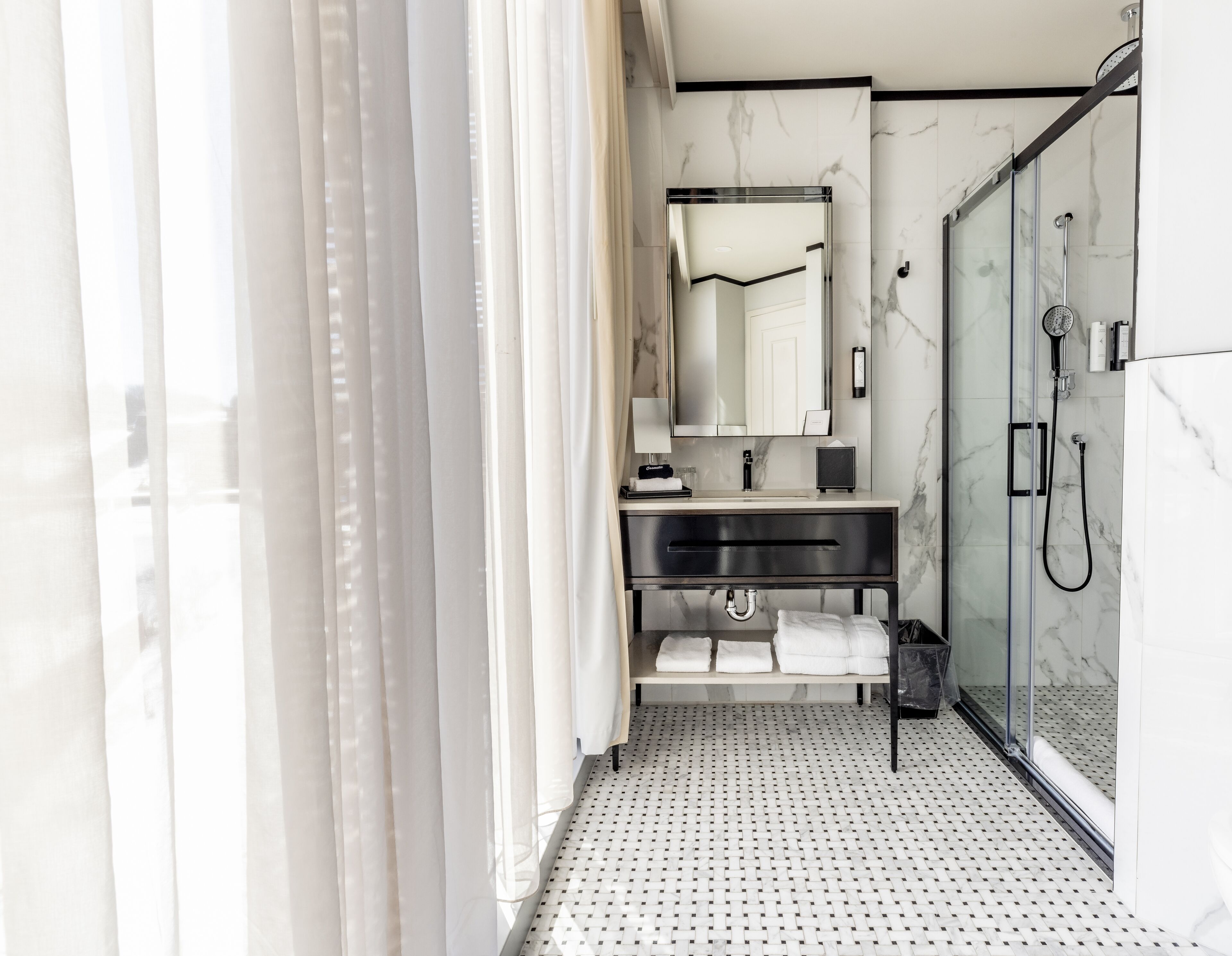 Un baño moderno con cabina de ducha de vidrio, suelo de baldosas de mármol y un lavabo con espejo y toallero.