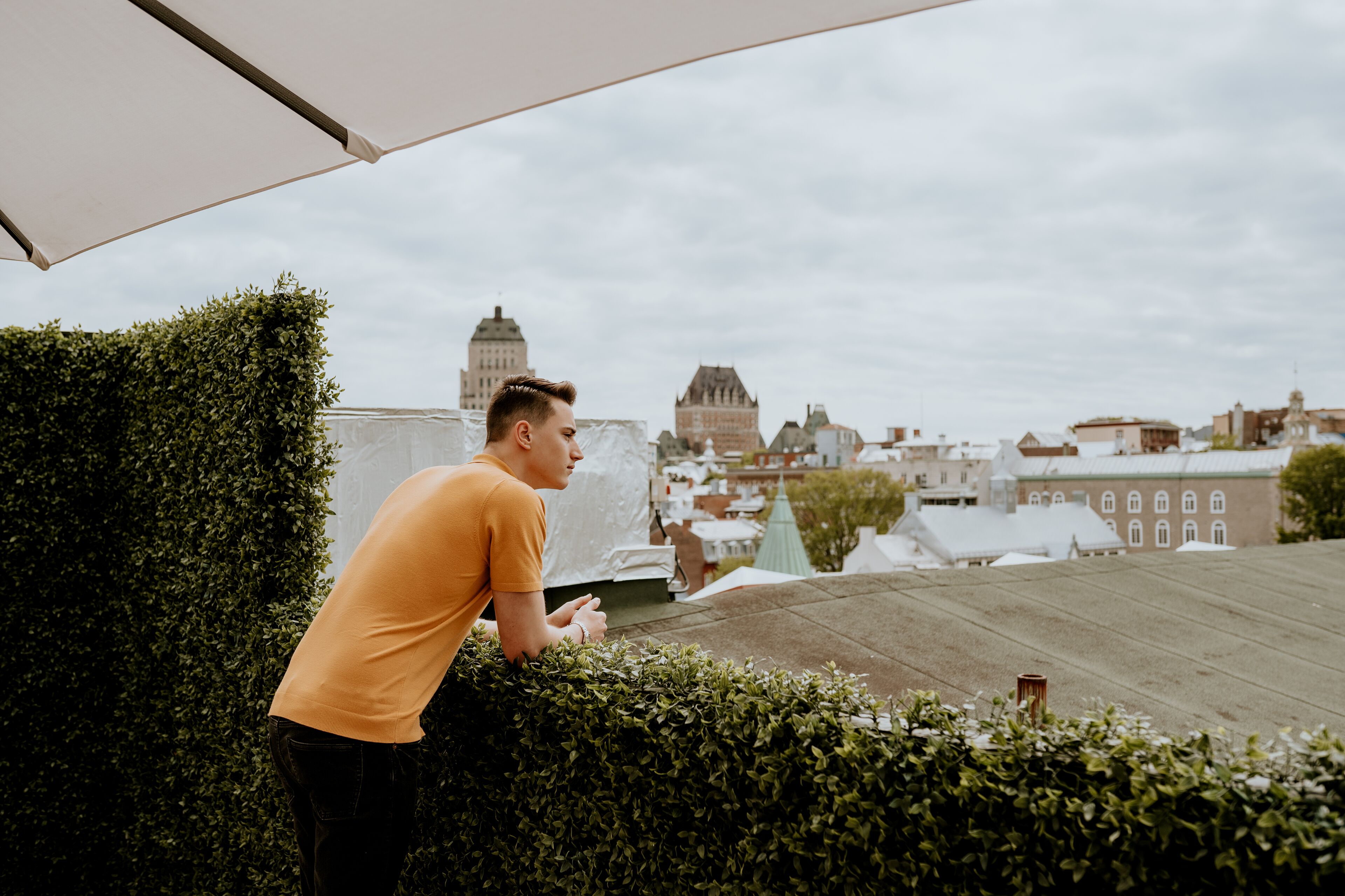 A person leaning on a rooftop railing overlooking a cityscape with historic buildings.