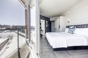 Una habitación de hotel moderna con una cama grande, un balcón con vistas a la ciudad y un ventanal amplio.