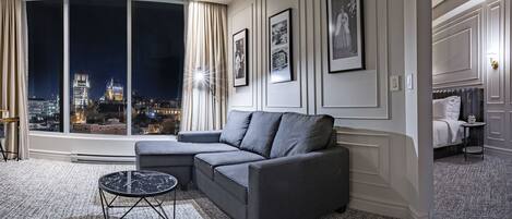 A modern living room with a grey sofa, a round coffee table, and a large window with a city view at night.