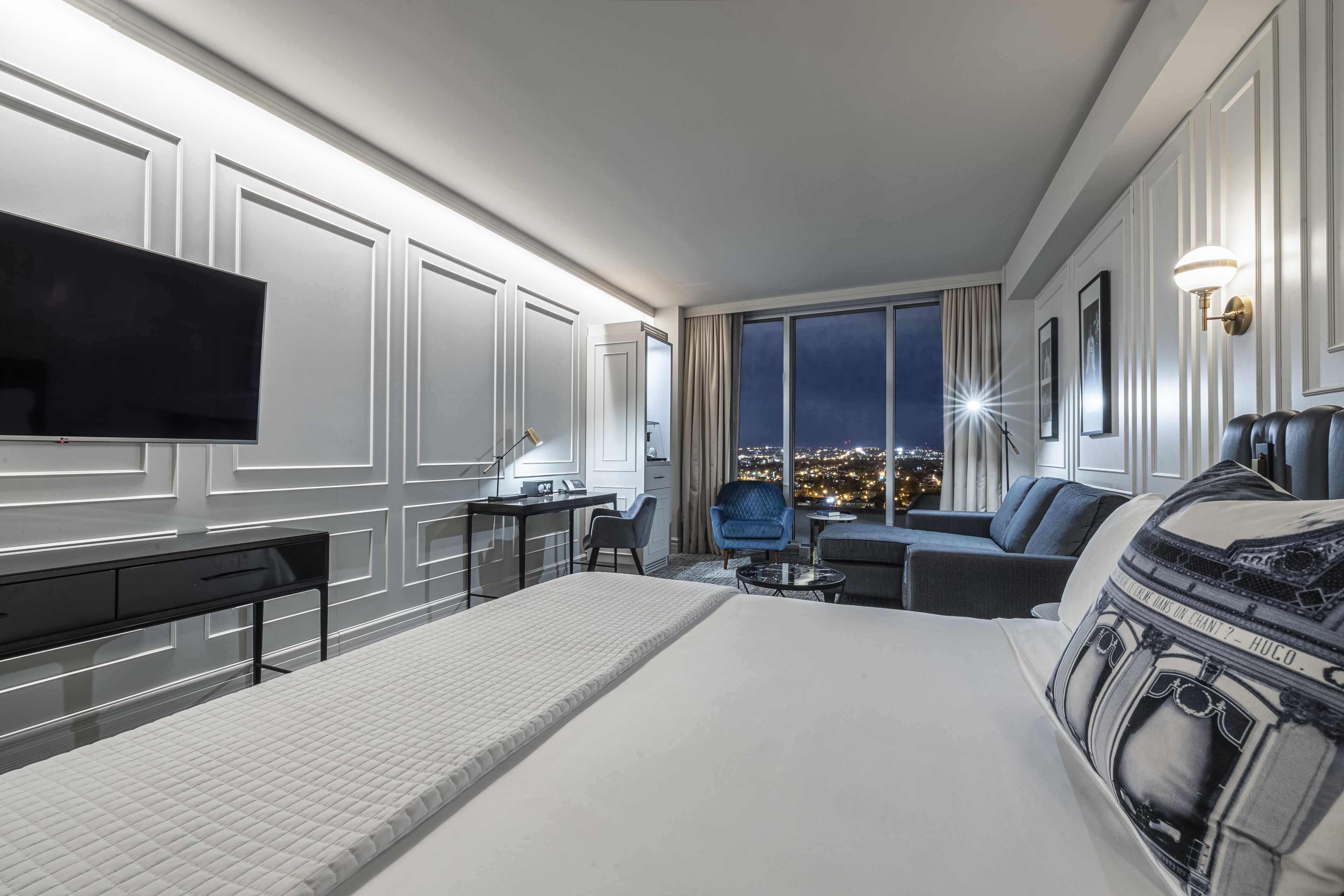 A hotel room with a large bed, a desk, a chair, a sofa, and a TV.