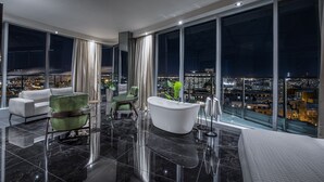 A modern hotel room with a large city view, a bathtub, and a green armchair. - Le Capitole Hôtel (Québec City)