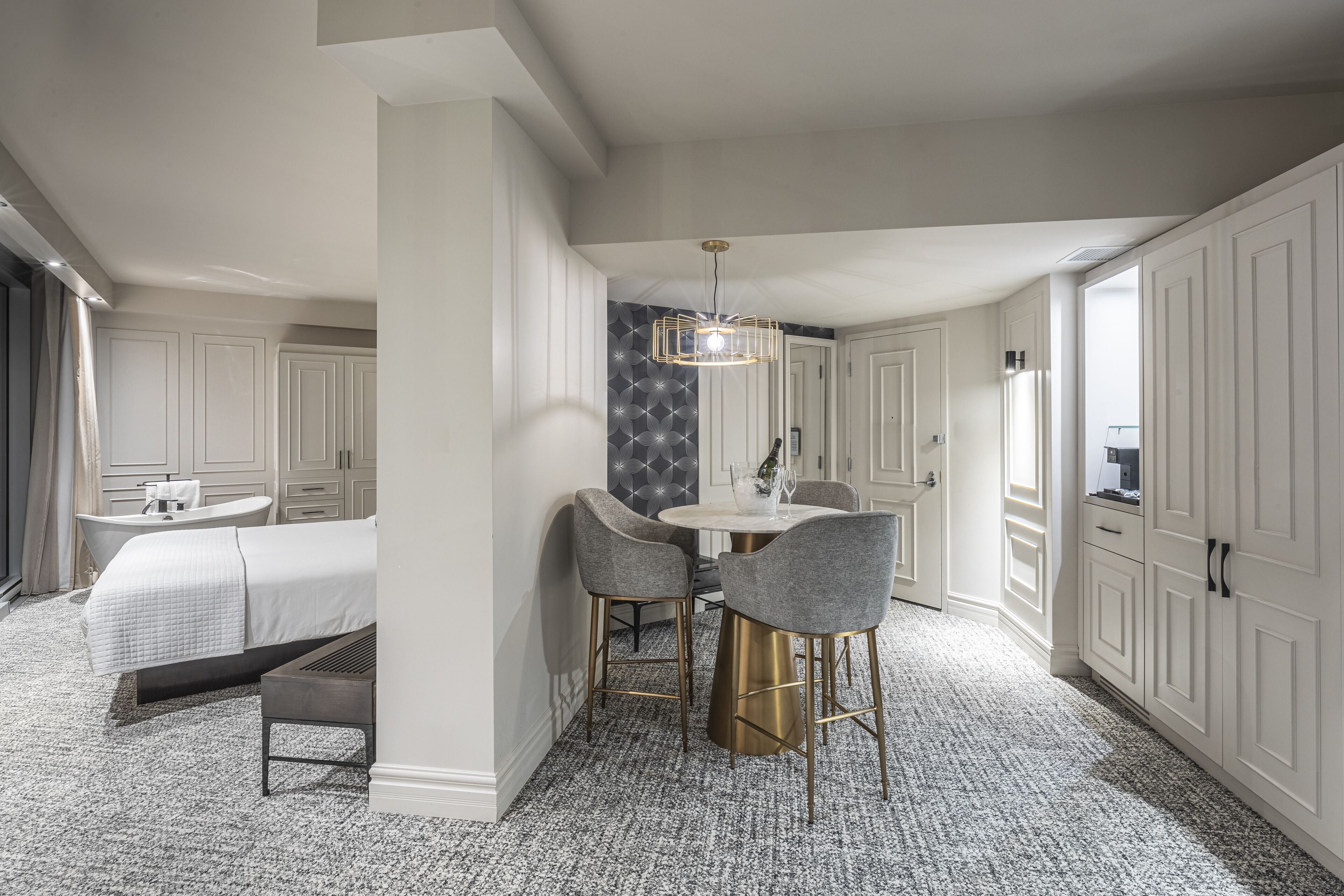A hotel room with a bed, a bathroom, a dining area with a table and chairs, and a large wardrobe.