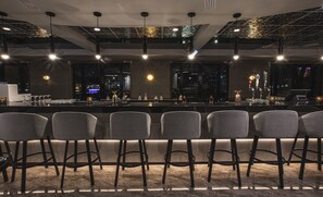 A bar area with a city view, bar stools, and a well-lit ceiling.