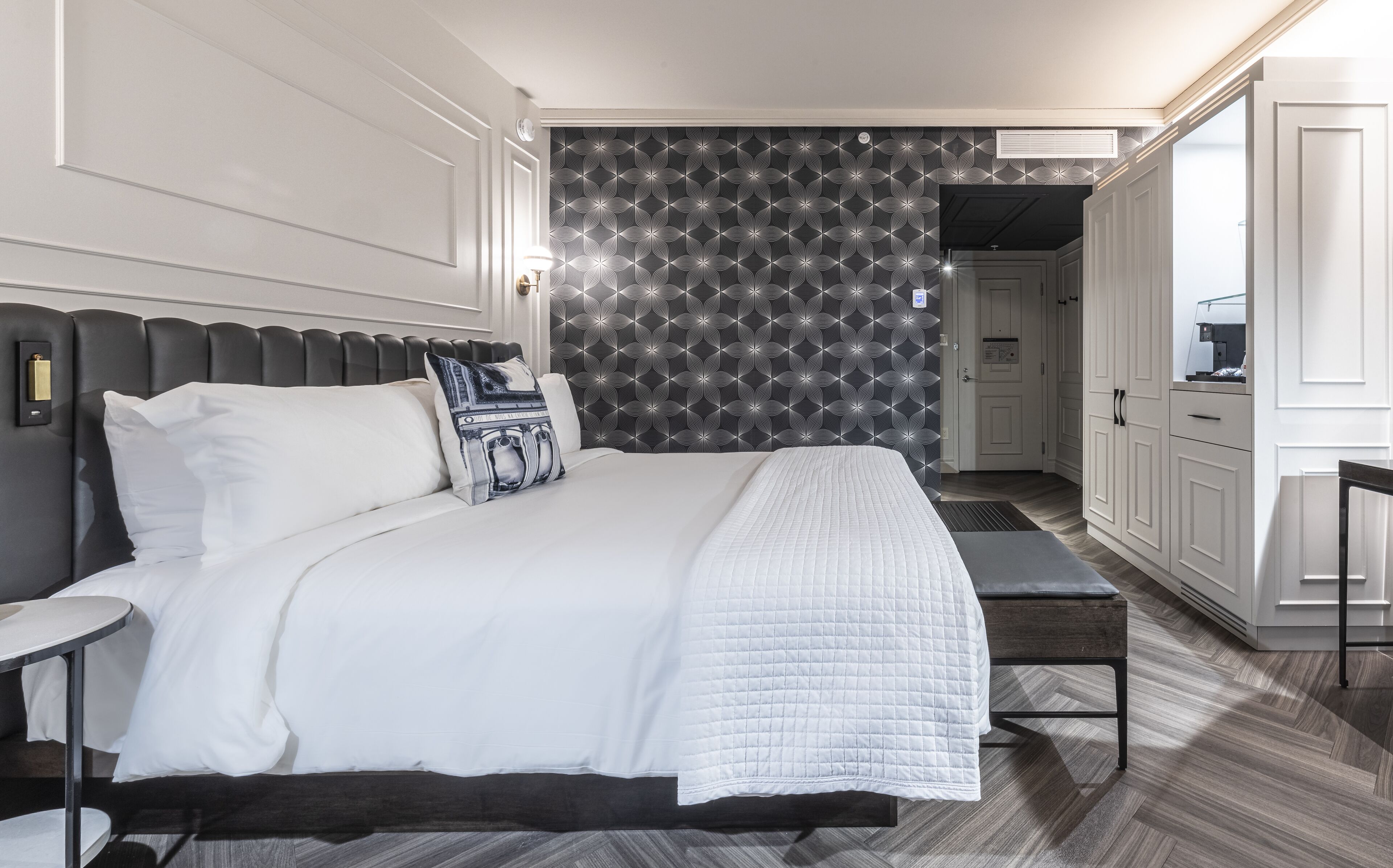 Ein modernes Hotelzimmer mit einem großen Bett, einem Nachttisch, einer Bank und einem Kleiderschrank.