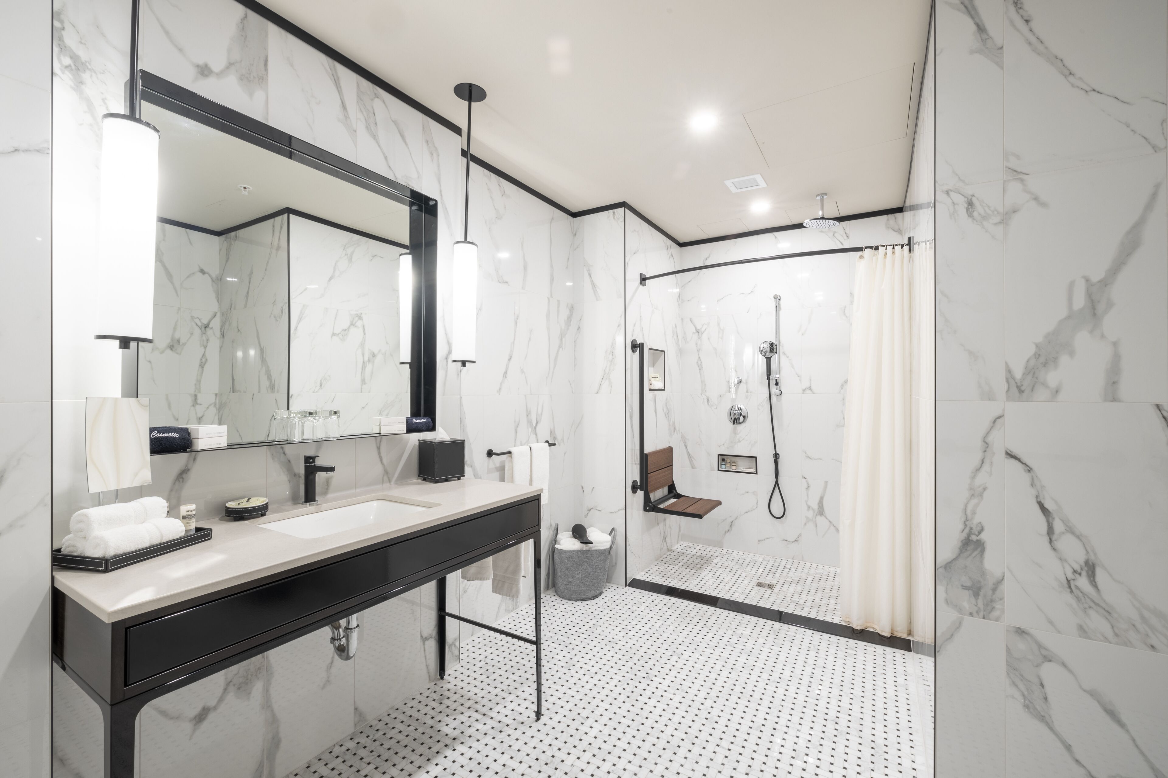 Un baño moderno con un espejo grande, encimera negra y zona de ducha con puerta de cristal.