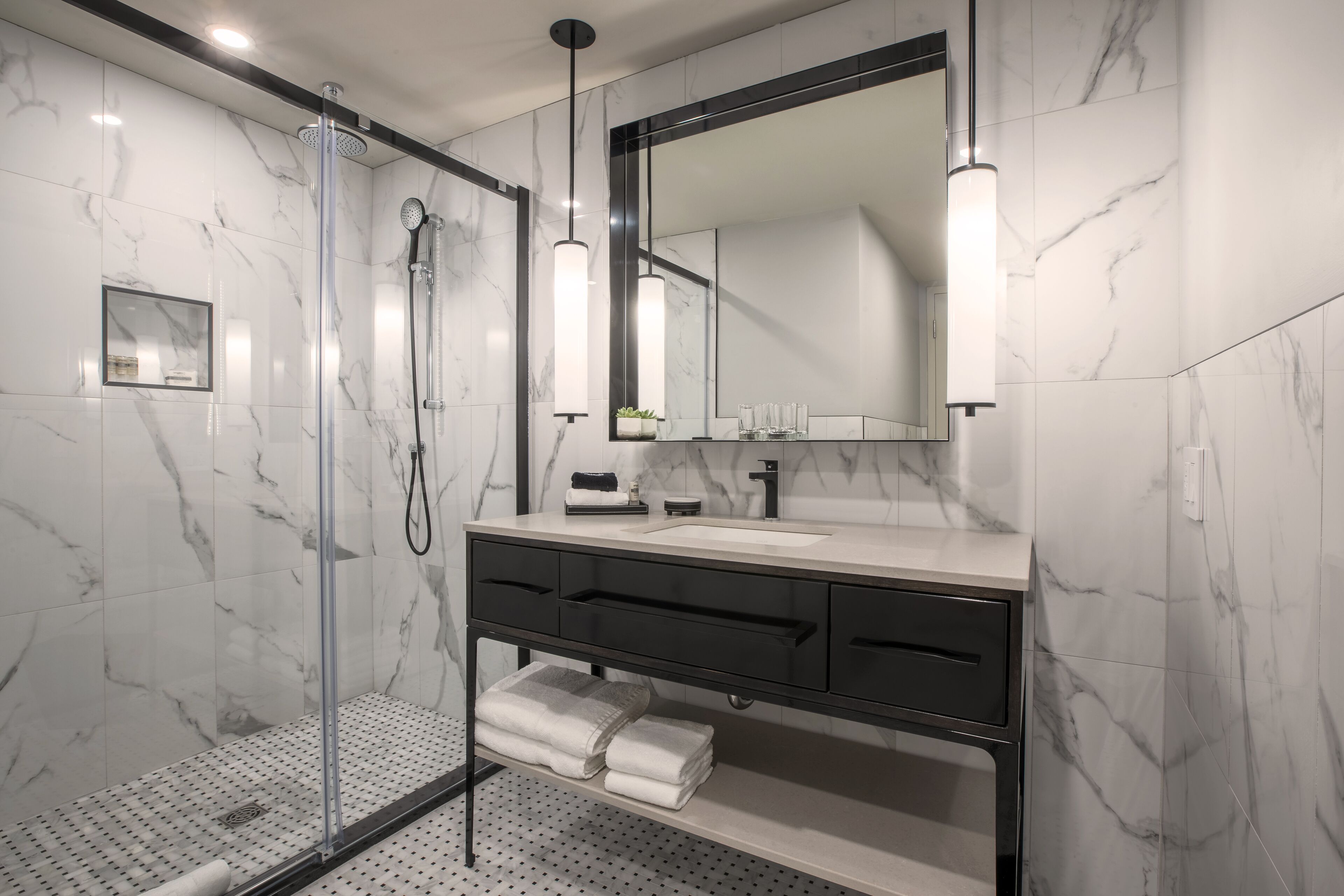 Un baño moderno con ducha de vidrio, un espejo grande y pared con azulejos de mármol.