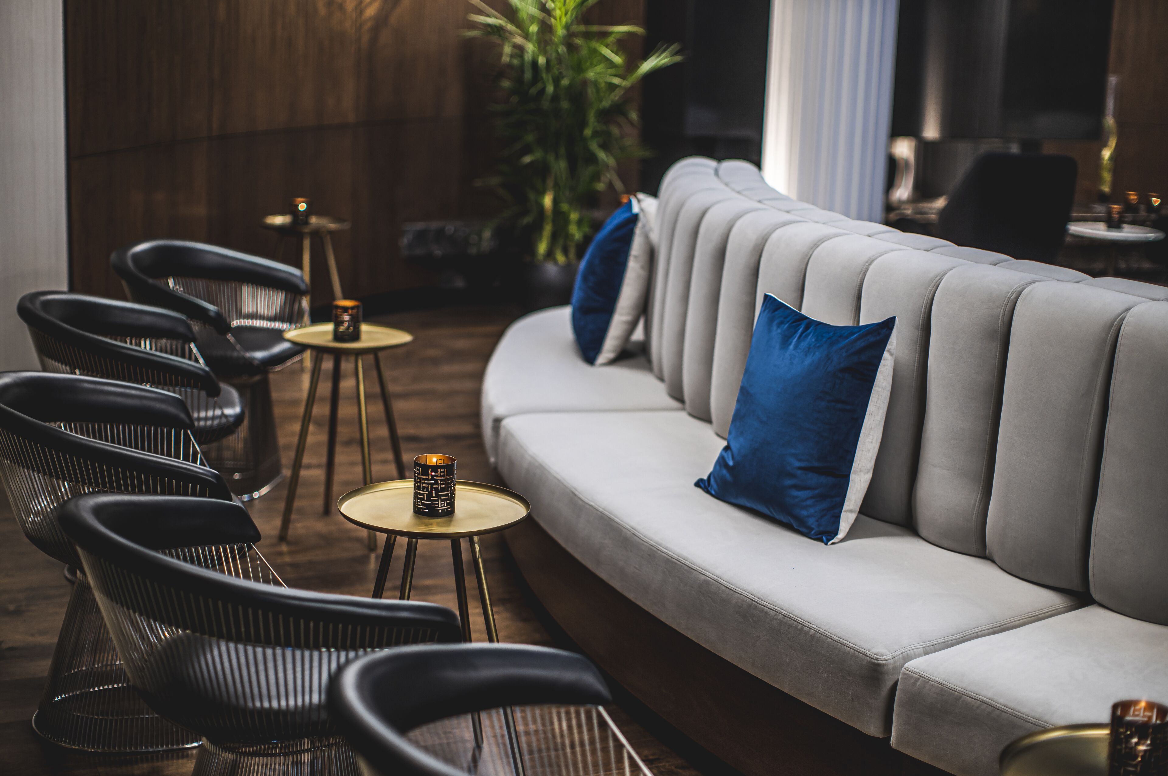 Un espace détente moderne avec un canapé gris, des fauteuils noirs et de petites tables rondes ornées de bougies.