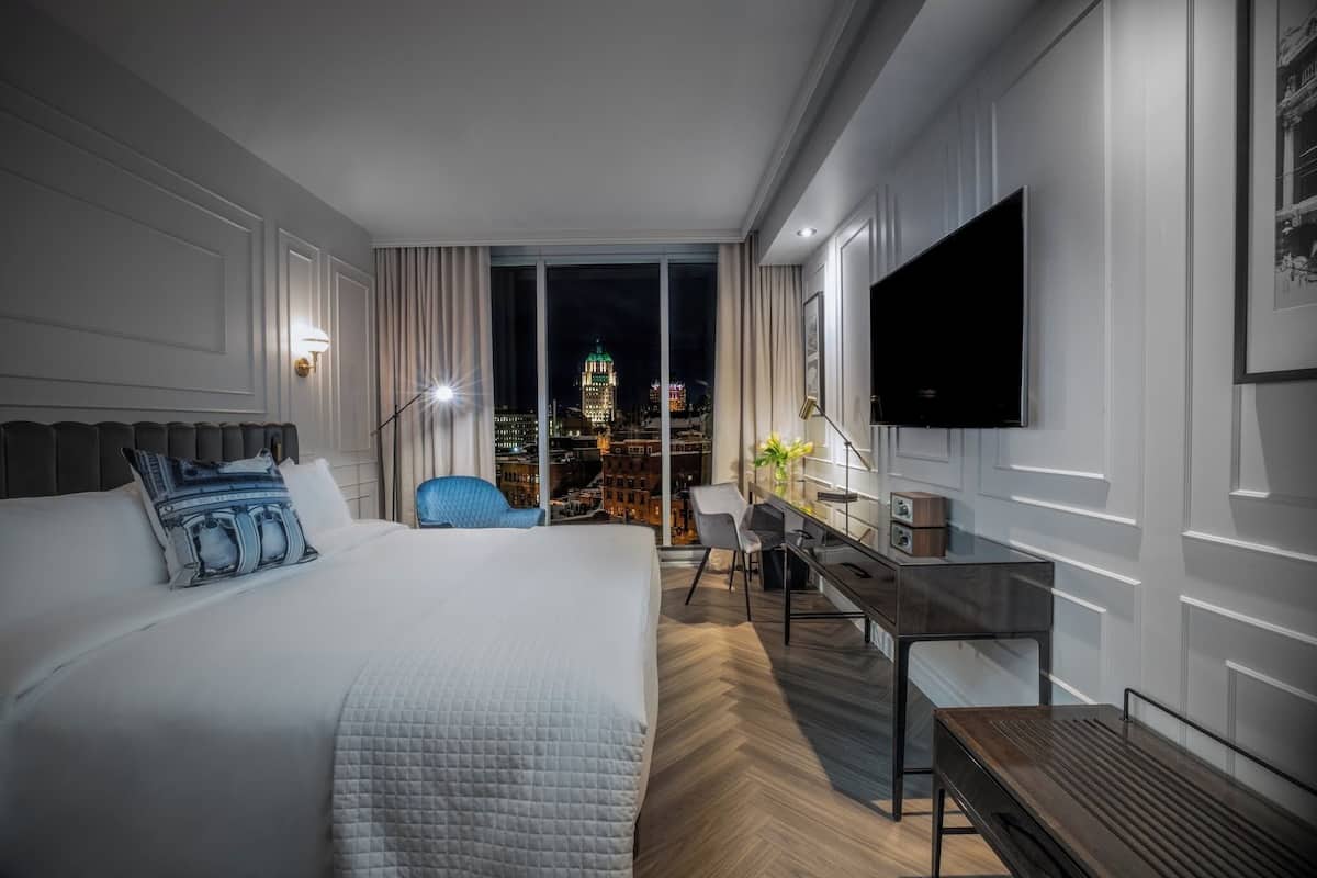 Moderni hotellihuone, jossa on suuri sänky, työpöytä, tuoli ja televisio.