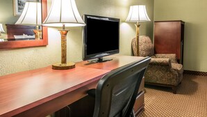 A hotel room with a wooden desk, two lamps, a television, a patterned armchair, and a cabinet. - Quality Inn & Suites Ann Arbor Hwy 23 (Ann Arbor)